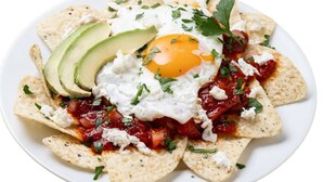 A plate of nachos topped with avocado slices, a fried egg, and cheese, garnished with herbs. - Hotel Villa Vitta (Bahia de los Angeles)