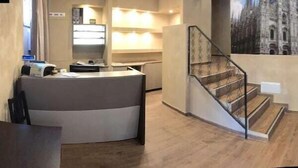 Vestíbulo de hotel con mostrador de recepción, una escalera y un gran mural de una catedral.