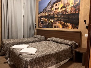 A hotel room with two beds, a nightstand, a painting of a bridge, and a window with curtains.