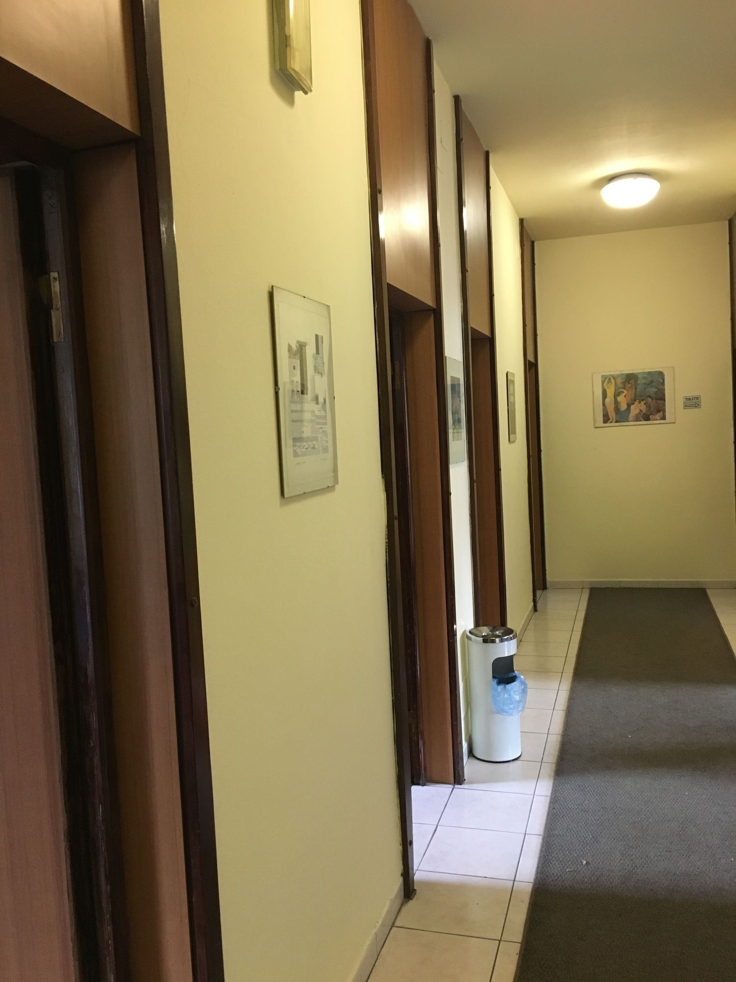 Un corridoio con porte di legno, un cestino e due quadri appesi alle pareti.