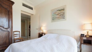 Ein Hotelzimmer mit einem großen Bett, einem Holzschrank, einem Schreibtisch mit Lampe sowie einem Bild an der Wand.