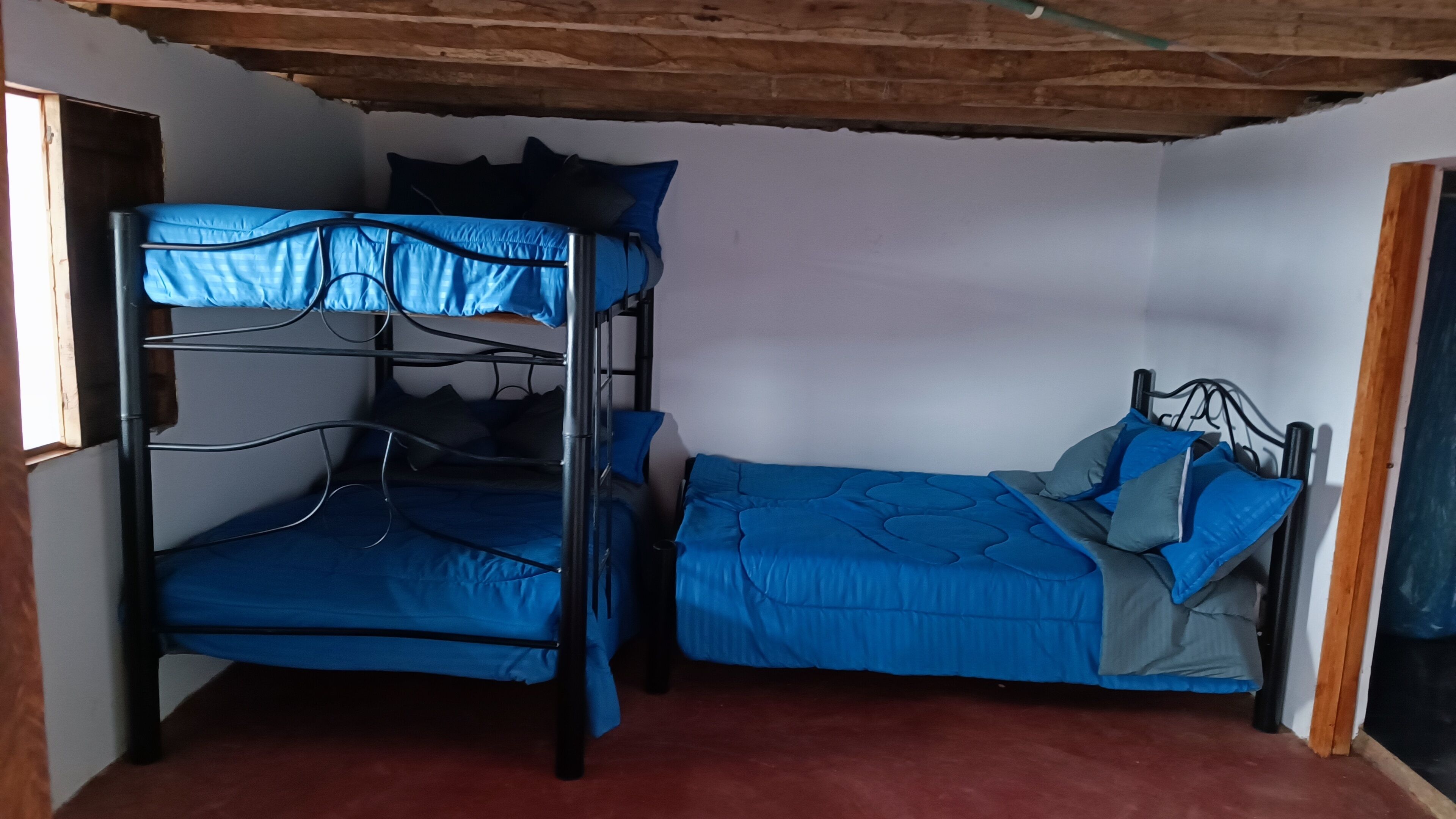A room with two bunk beds, one with a metal frame and the other with a wooden frame, both with blue bedding.