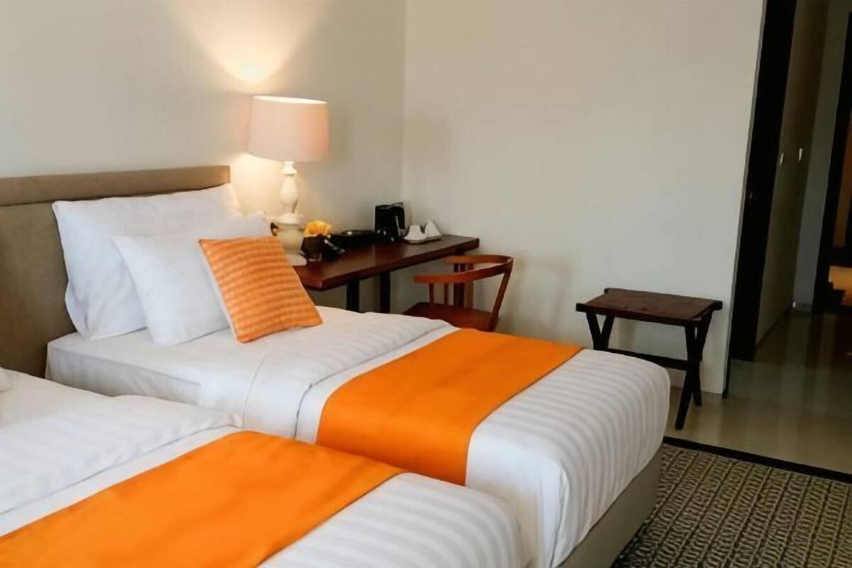 A hotel room with two beds, a desk, a chair, and a small table.