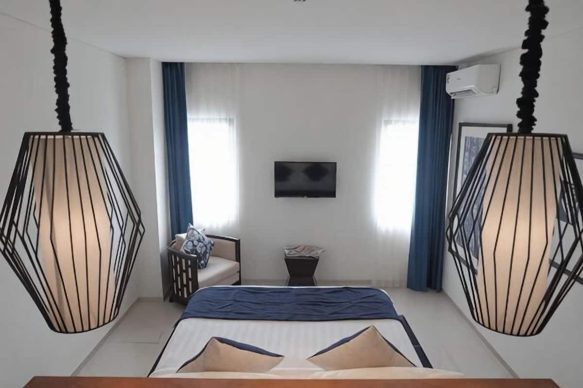A bedroom with a bed, two hanging lamps, a TV on the wall, and a window with curtains.