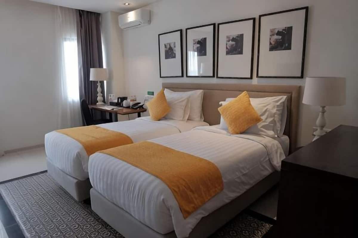 A hotel room with two beds, a nightstand, a desk, and a chair.