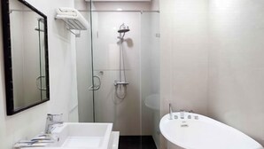 A modern bathroom with a freestanding bathtub, a large mirror, and a glass-enclosed shower area. - M Hotel Sorong Managed by East Season (Sorong)