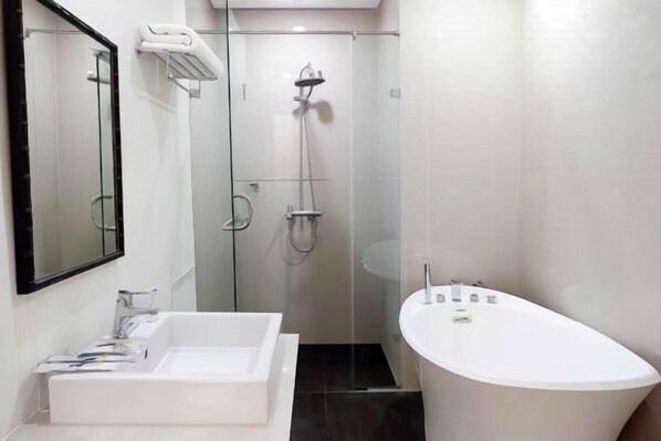 A modern bathroom with a freestanding bathtub, a large mirror, and a glass-enclosed shower area. - M Hotel Sorong Managed by East Season (Sorong)