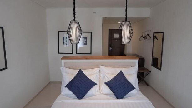 A modern hotel room with a bed, two pendant lights, a wooden headboard, and framed pictures on the walls. - M Hotel Sorong Managed by East Season (Sorong)