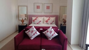 A hotel room with a bed, two bedside tables, a red sofa, and a large mirror. - M Hotel Sorong Managed by East Season (Sorong)