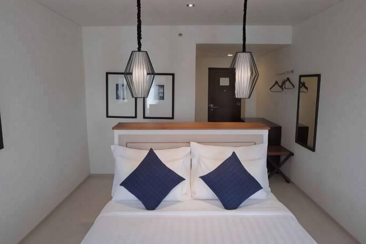 A bedroom with a bed, two pillows, a wooden headboard, and two hanging pendant lights.