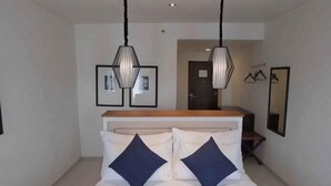 A bedroom with a bed, two pillows, a wooden headboard, and two hanging pendant lights. - M Hotel Sorong Managed by East Season (Sorong)