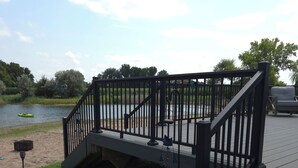 A wooden deck with a black railing, a small boat on the water, and a chair in the background. - Charming 3-bedroom house in Gibbon with waterfront views Crane central (Gibbon)