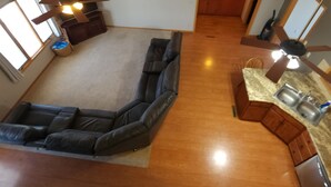 A high-ceilinged living room with a sectional sofa, a ceiling fan, and a kitchen area with wooden cabinets and a sink. - Charming 3-bedroom house in Gibbon with waterfront views Crane central (Gibbon)