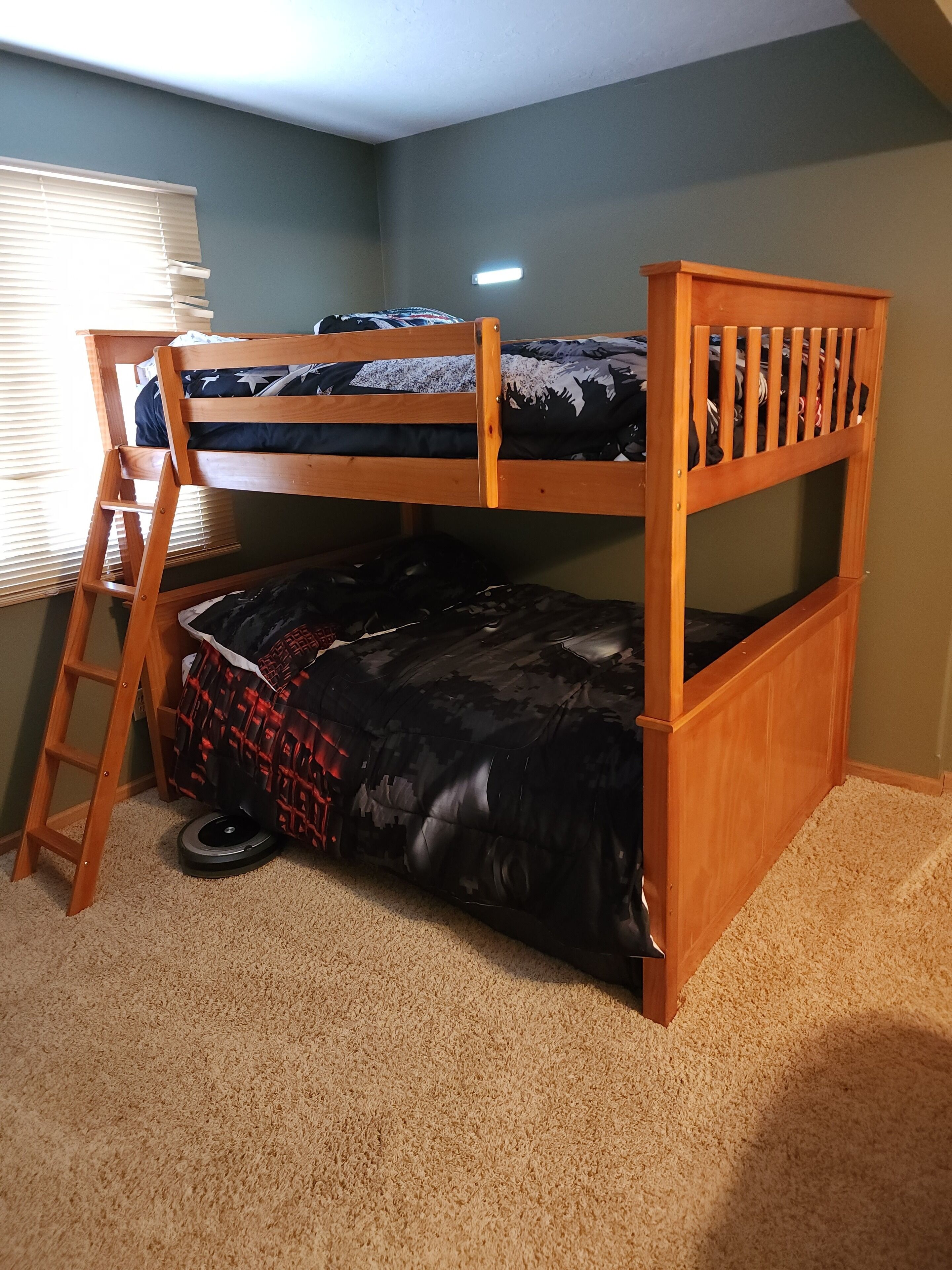 A bunk bed with a ladder, a small window with blinds, and a carpeted floor.