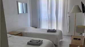 Una camera d'albergo con due letti, un comodino, una lampada e una finestra con tende.
