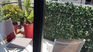 Un balcone con due sedie bianche, una pianta in vaso e un grande siepe.
