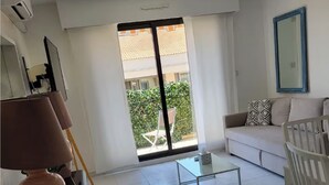 Un soggiorno moderno con un divano, un tavolino e un mobile TV. Si vede una grande finestra con vista su un balcone e del verde all'esterno.