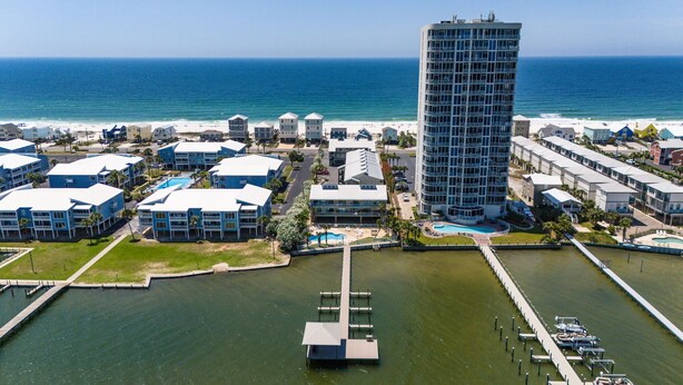 Un hotel costero con un edificio central, un puerto deportivo y una playa al fondo.
