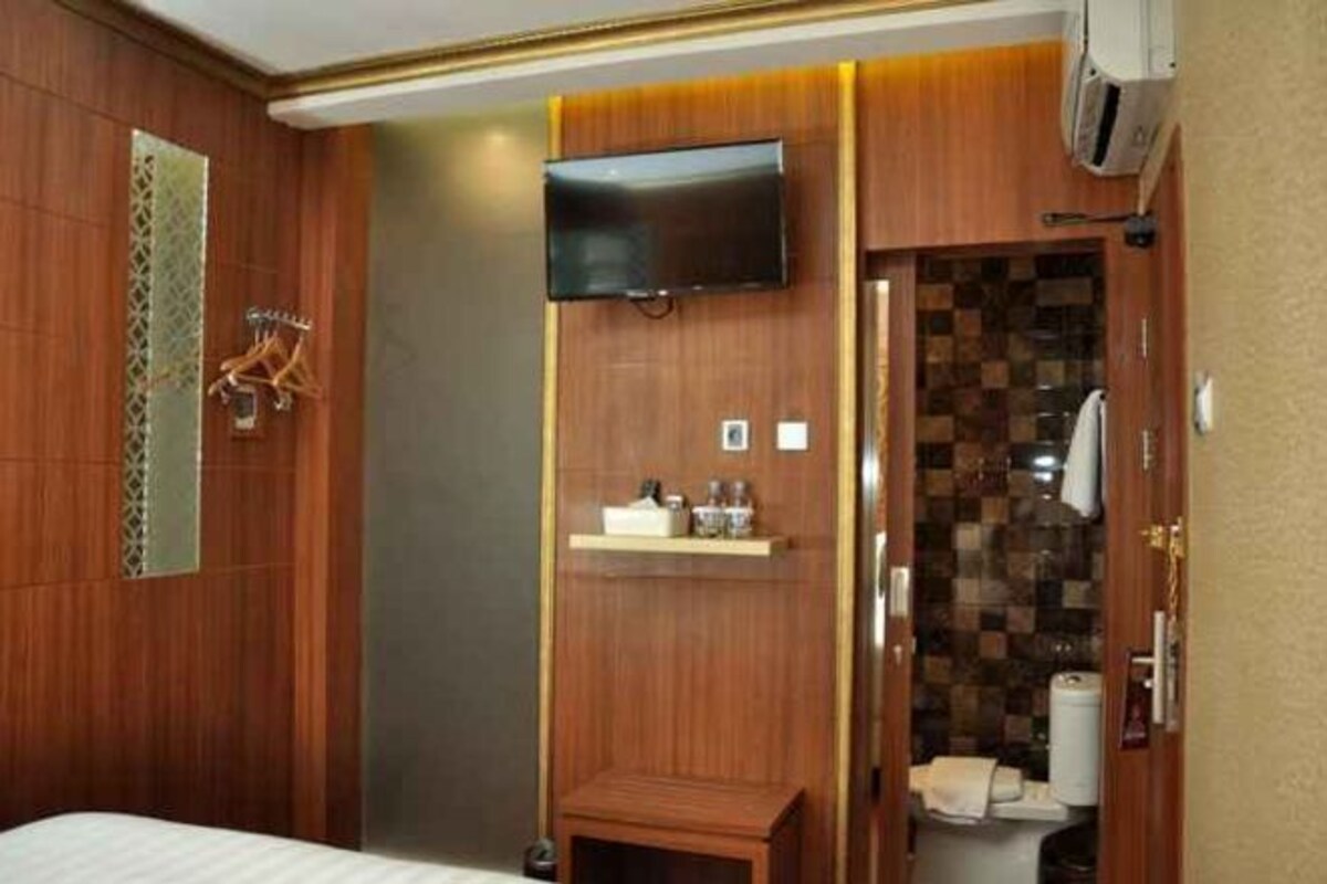 Un baño de hotel con tocador de madera, un televisor montado encima y zona de ducha con pared de azulejos.