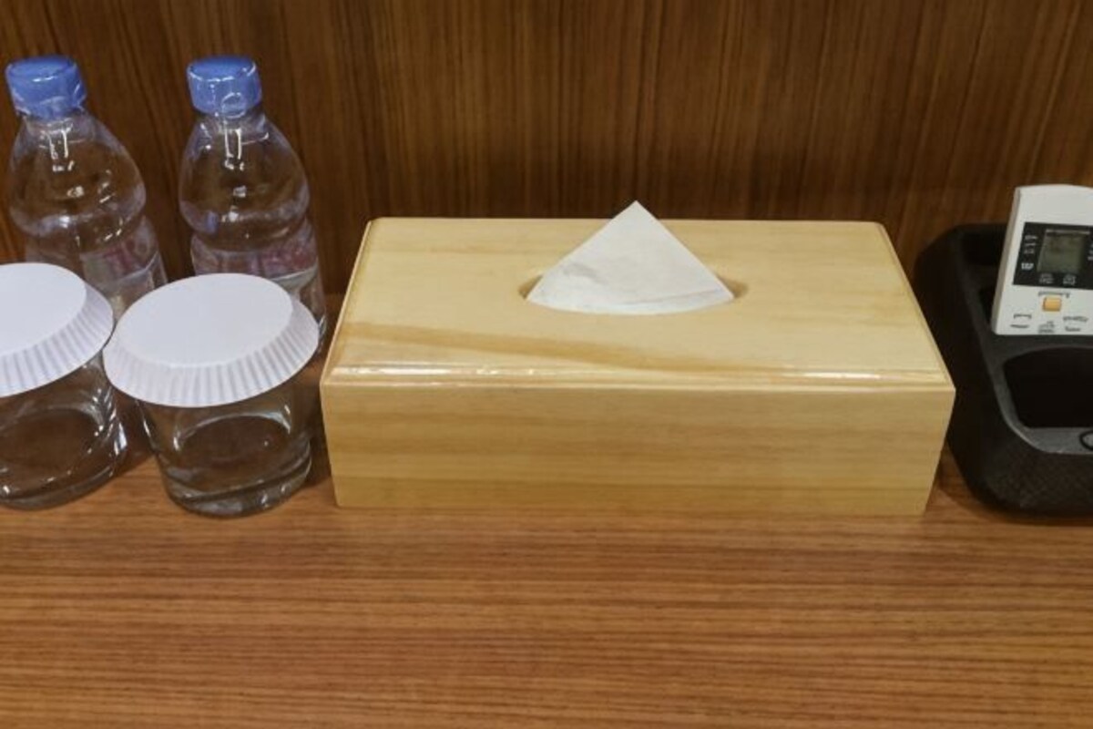 A wooden box with a tissue, three bottles with caps, and a device on a wooden surface.