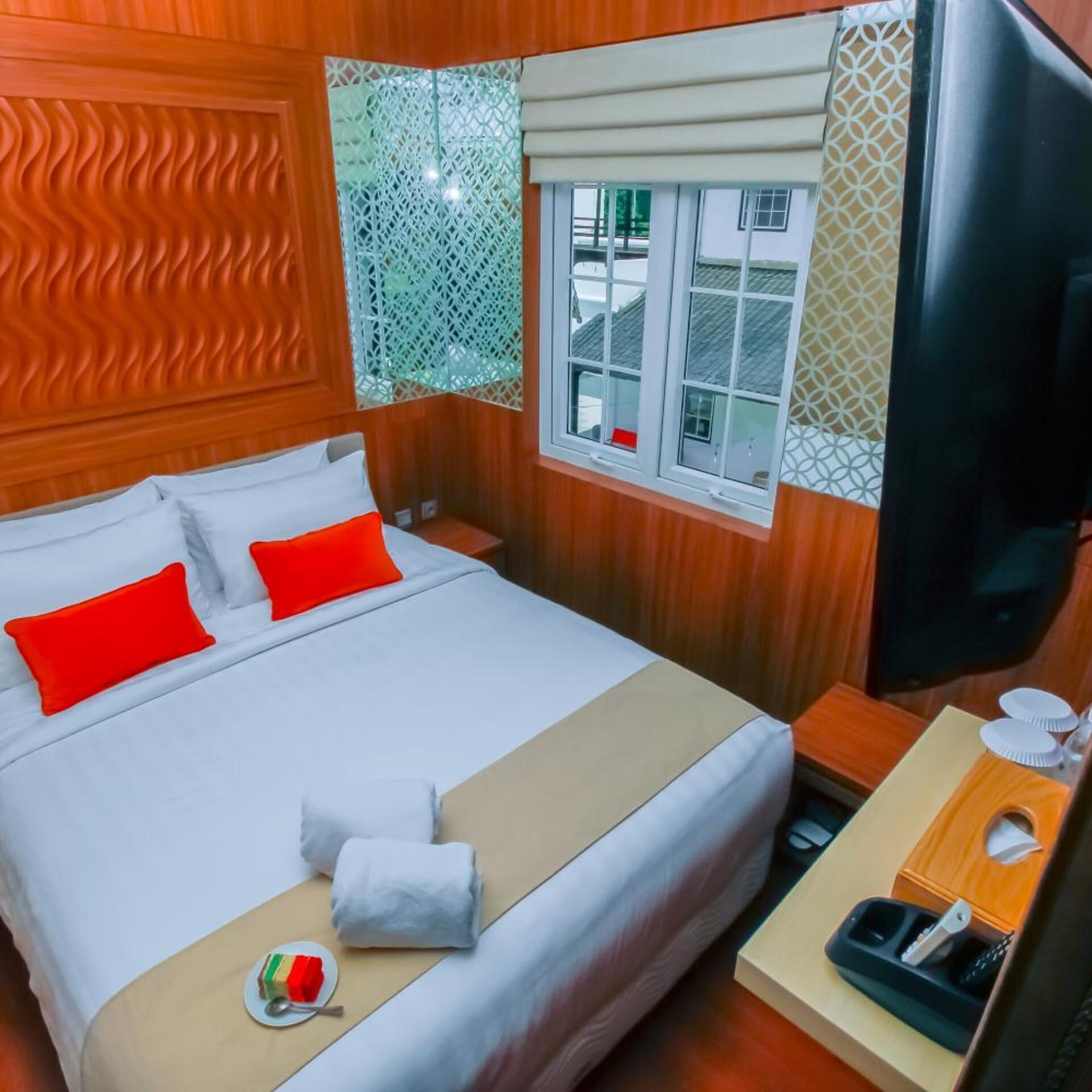 Una habitación de hotel con una cama, un televisor, una mesita de noche y una ventana con cortinas.
