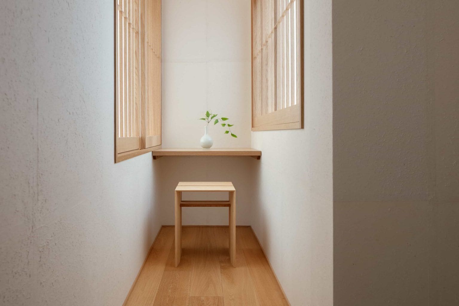 A small, narrow room with a wooden bench and a white vase with a plant on a shelf.