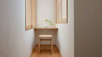 A small, narrow room with a wooden bench and a white vase with a plant on a shelf.