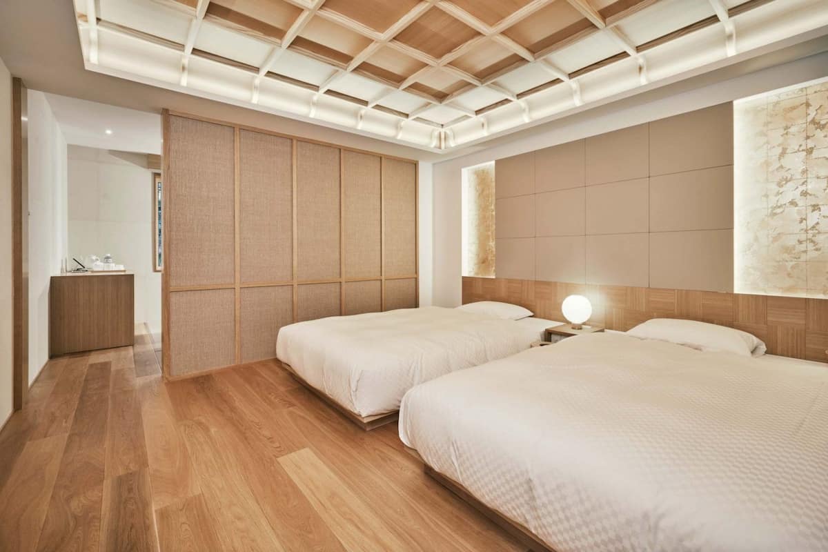 A hotel room with two beds, a wooden ceiling, and a large abstract painting on the wall.