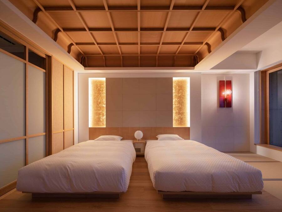 Quarto de hotel moderno com duas camas, piso de madeira, teto inclinado e grandes janelas.