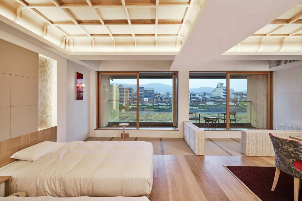 A modern hotel room with a large bed, a seating area with a view, and large windows.