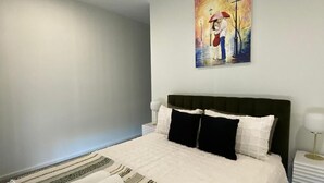 Ein ordentlich bezogenes Bett mit gestreiftem Überwurf und Kissen, ein Deckenventilator, ein Bild an der Wand und ein Nachttisch mit einer Lampe.