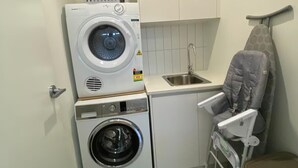 Ein kleiner Waschbereich mit zwei übereinander gestapelten Waschmaschinen, einem kleinen Waschbecken und einem Wäscheständer.