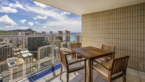 Een balkon met een tafel en stoelen, met uitzicht op een stadsgezicht en de oceaan.