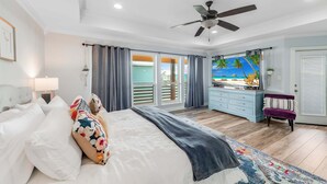 A bedroom with a bed, a ceiling fan, a nightstand, a dresser, a chair, and a view of the outdoors.