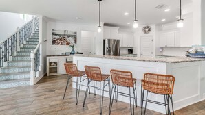 A modern kitchen with white cabinetry, a stainless steel refrigerator, and a central island with bar stools.