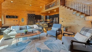 A spacious living area with a wooden ceiling, a sofa set, a coffee table, and a staircase leading to an upper level. - Mountain Solace - Pet Friendly | Hot Tub | Shuffleboard and Arcade Games (Blue Ridge)