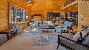A spacious living room with a large window, a dining area, and a kitchen. - Mountain Solace - Pet Friendly | Hot Tub | Shuffleboard and Arcade Games (Blue Ridge)