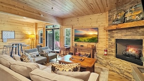 A cozy log cabin interior with a fireplace, a television, and a sofa. - Mountain Solace - Pet Friendly | Hot Tub | Shuffleboard and Arcade Games (Blue Ridge)