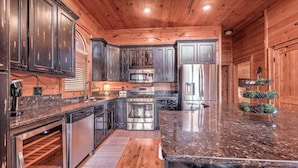 A modern kitchen with dark wooden cabinets, stainless steel appliances, and a marble countertop. - Mountain Solace - Pet Friendly | Hot Tub | Shuffleboard and Arcade Games (Blue Ridge)