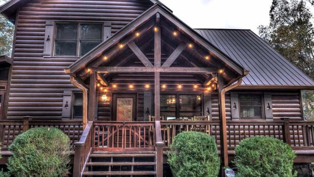 A log cabin with a porch, wooden railings, and string lights.