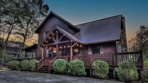 A log cabin with a porch, wooden railings, and string lights.