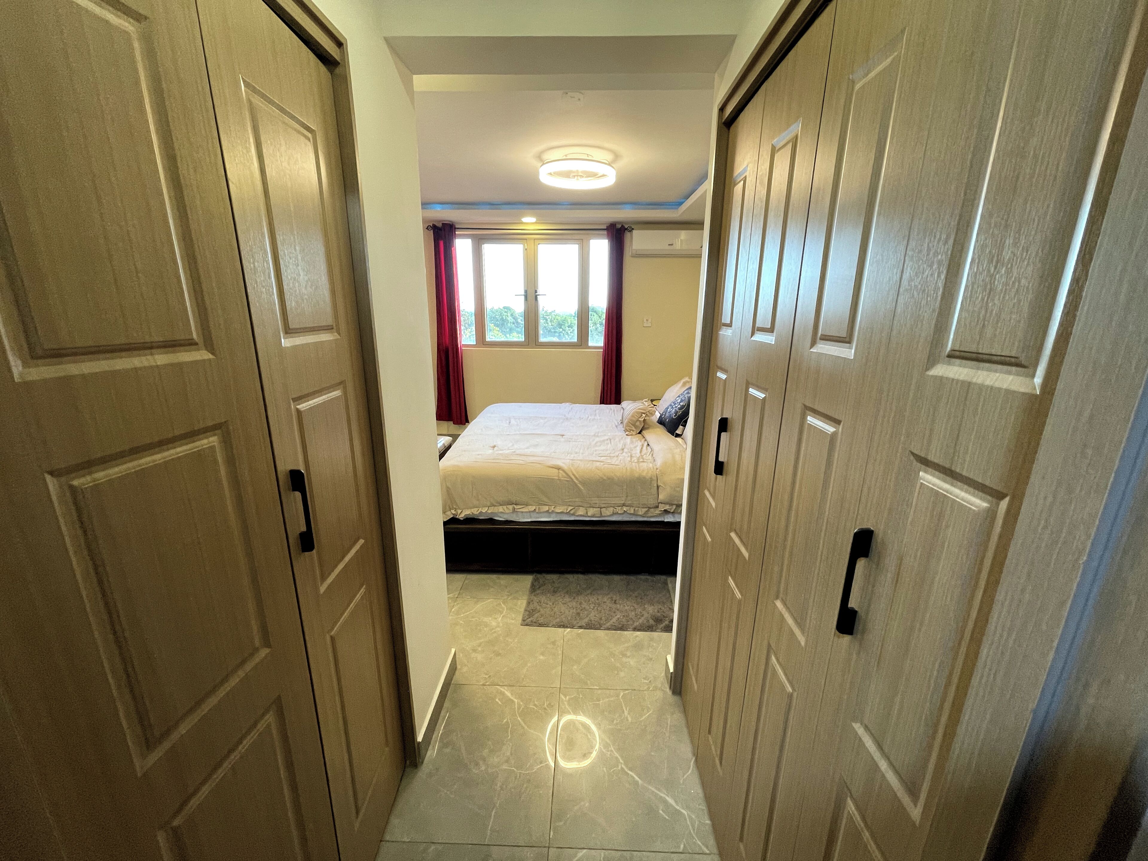 Un dormitorio con una cama, una ventana con cortinas y una puerta que da a otra habitación.