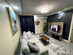 A living room with a sofa, coffee table, TV, and artwork on the wall. - Modern Chic Apartment Suite With Pool & Ocean View with AC, WiFi in Kingston (Kingston)