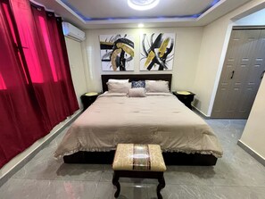 A bedroom with a large bed, two bedside tables, a bench, and abstract wall art. - Modern Chic Apartment Suite With Pool & Ocean View with AC, WiFi in Kingston (Kingston)