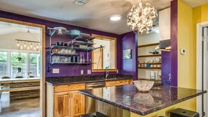 A modern kitchen with a granite countertop, wooden cabinets, and a unique chandelier. - Two-Home Heart of Austin Compound and Karaoke Room (Austin)