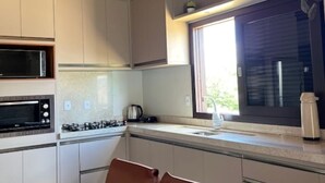 Une cuisine avec des meubles blancs, un four à micro-ondes, une cuisinière et une fenêtre donnant sur l’extérieur.