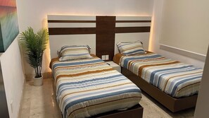 Two single beds with striped bedspreads are positioned against a wall with a headboard featuring horizontal slats.