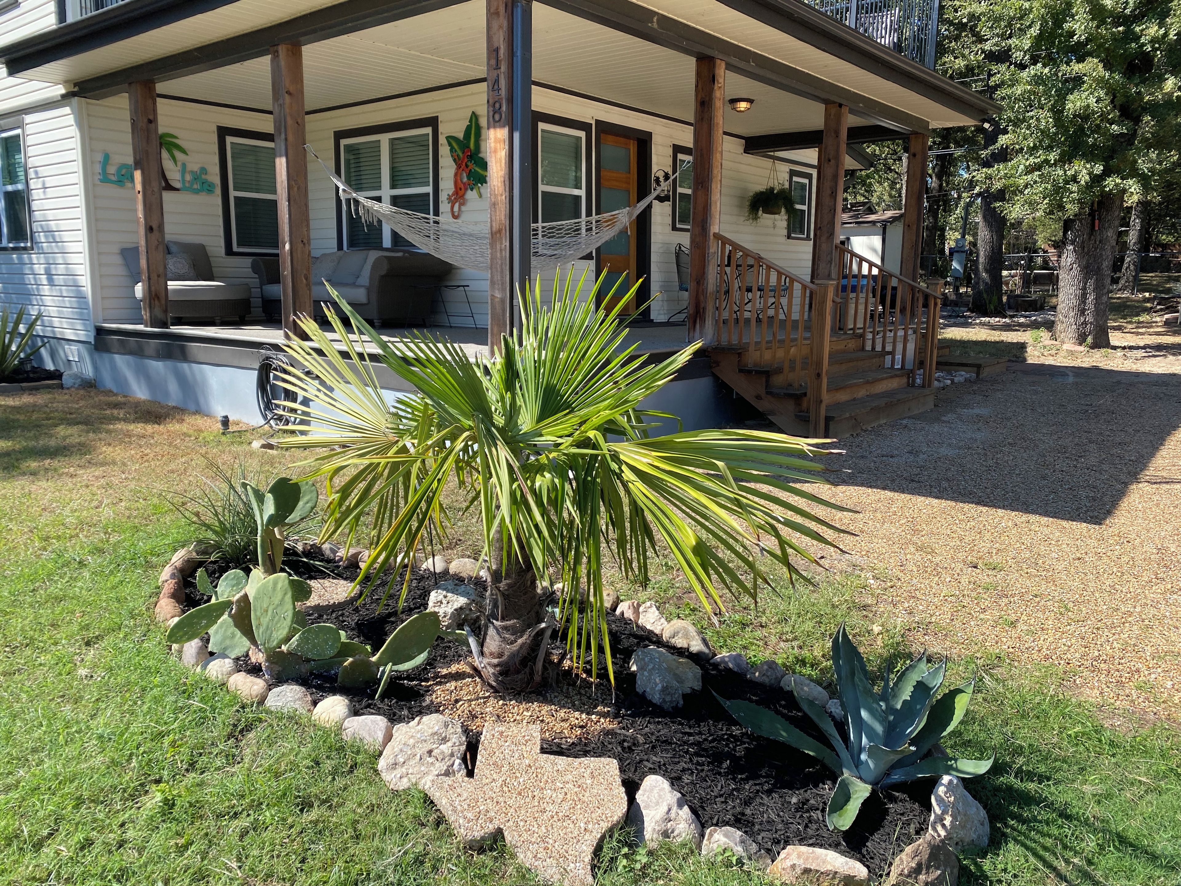 A house with a covered porch, a hammock, and a garden with cacti and agave plants.