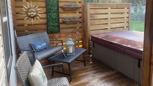 Een gezellig buiten zitgedeelte met een houten terras, een comfortabele bank en een kleine tafel met een lantaarn.