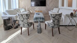 A modern living room with a large flat-screen TV mounted on a herringbone-patterned wall, a sofa, two patterned armchairs, a glass coffee table, and a small side table. - Views, Views, Views.Beautiful 2800 sqft 30 mins to Tahoe large backyard. (Reno)